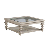Castlerock Cocktail Table, shown in light beige and warm taupe with wood, glass, and a inset glass top surface.